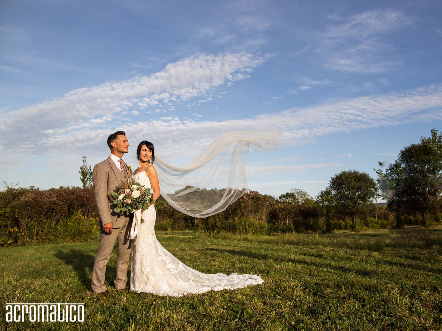 A bride and groom with the wind gently blowing the bride's veil and the blue sky behind them